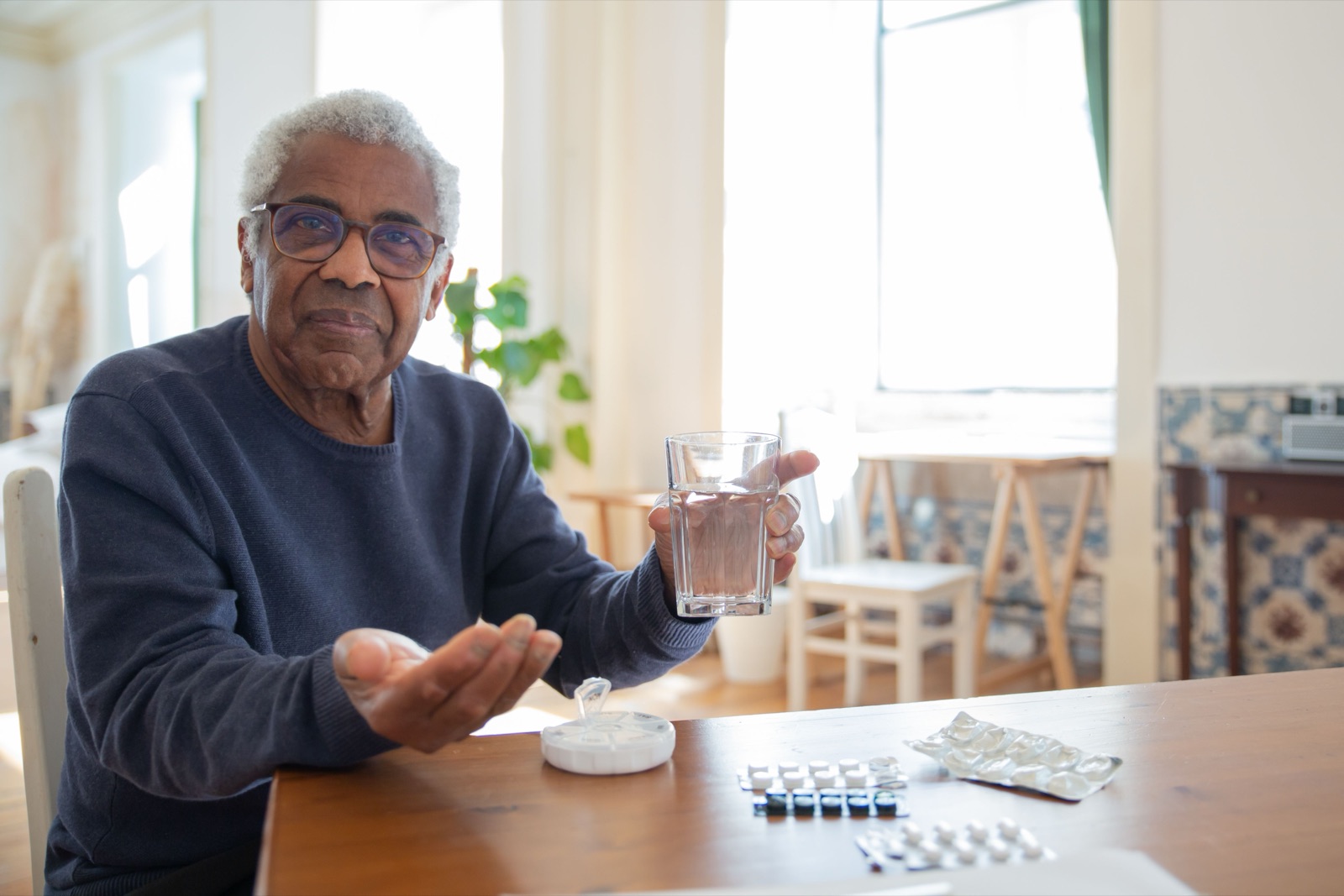 An older man at his table at home with a glass of water and his medication.