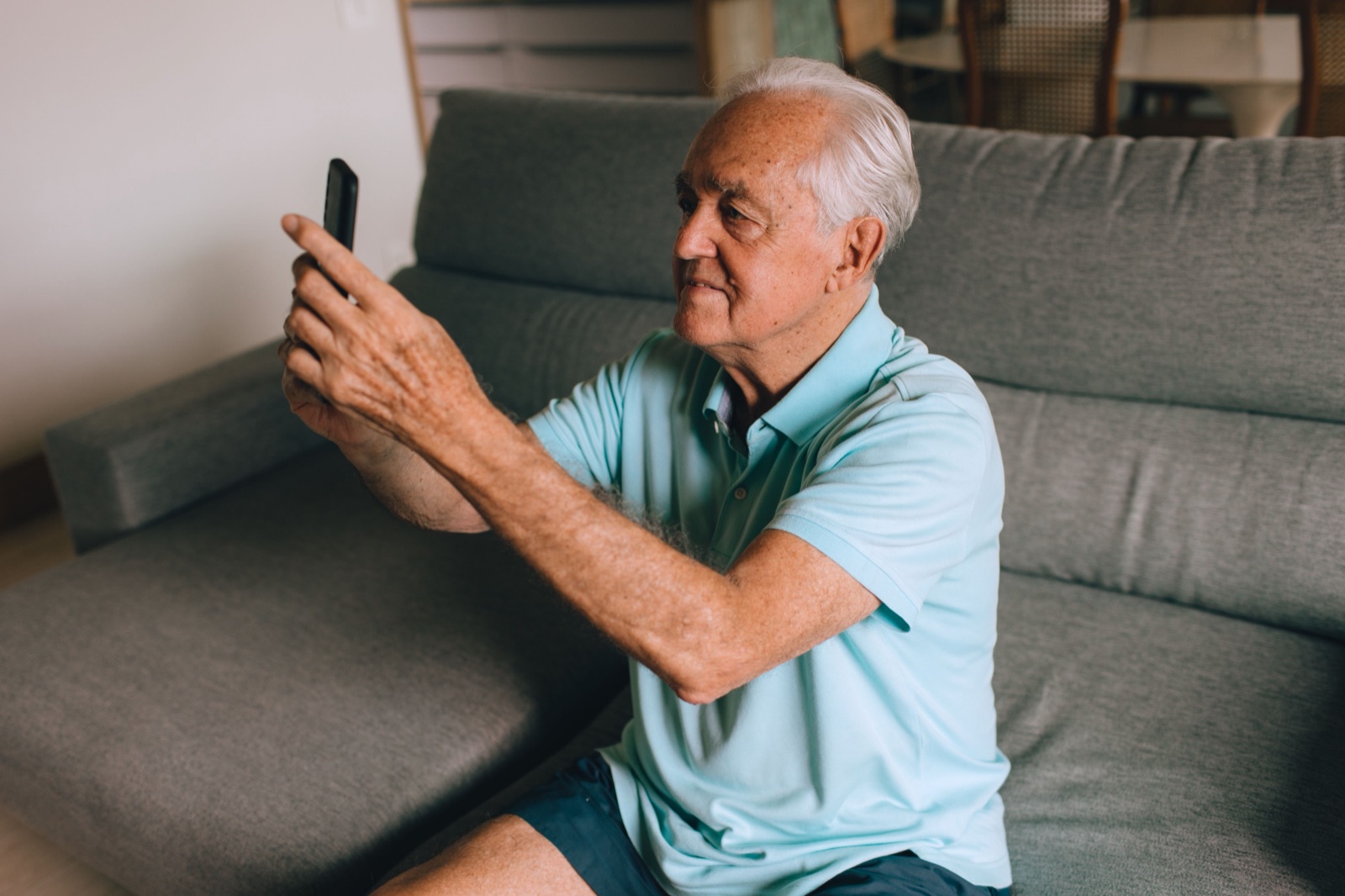 An older man on his couch at home, looking at his phone.