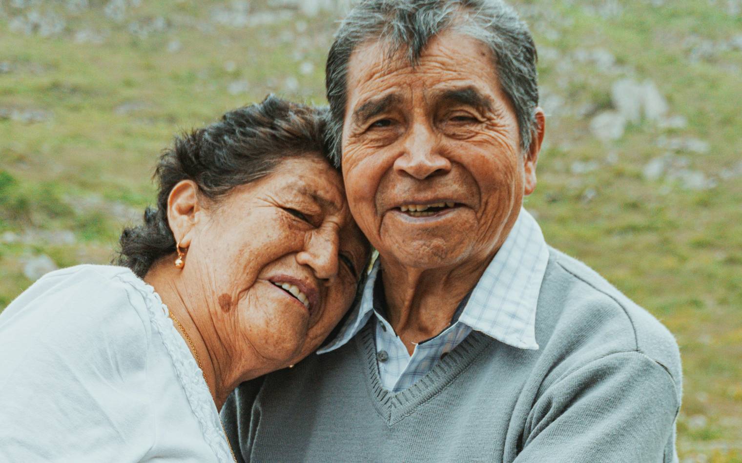 An older couple embracing on a hillside, her head on his shoulder.